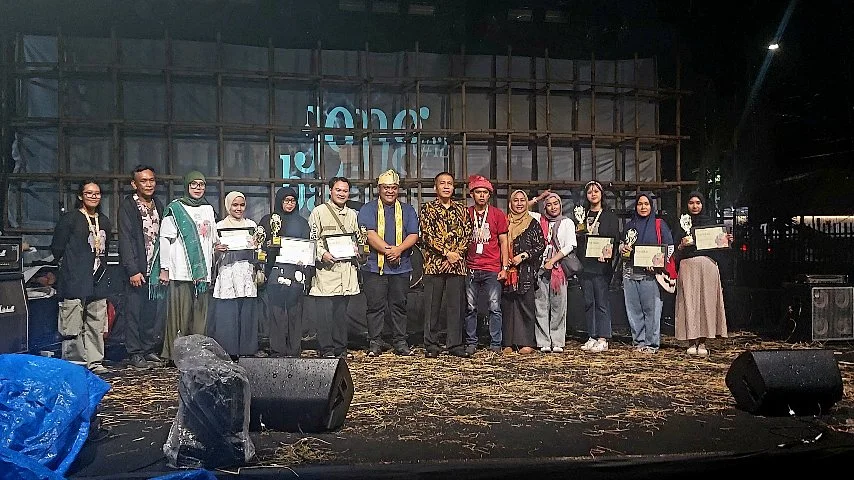 Sekelompok penerima penghargaan berpose di atas panggung usai acara penutupan Jong Batak Art Festival ke-12. Mereka memegang piala dan sertifikat sambil berfoto bersama panitia dan tamu undangan di depan latar bambu bertuliskan "Jong Batak".