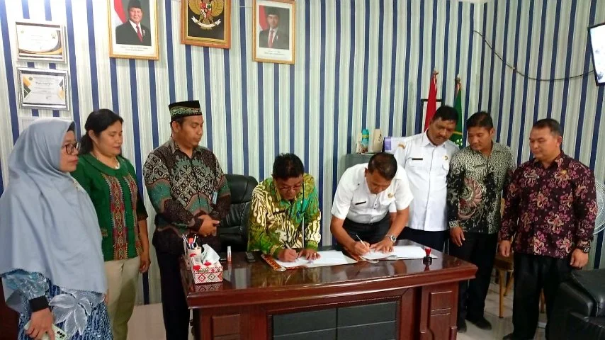 menampilkan momen formal penandatanganan dokumen yang melibatkan sembilan orang dewasa di sebuah ruangan kantor.