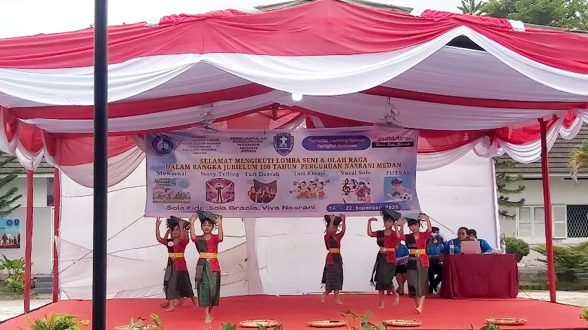 Sekelompok siswa SD menampilkan tarian tradisional di atas panggung berhias merah putih dalam lomba seni jubileum 100 tahun Perguruan Nasrani Medan.