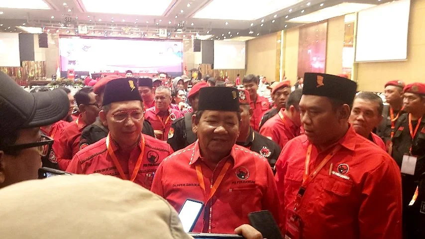 Sejumlah kader PDI Perjuangan mengenakan seragam merah dan kopiah hitam sedang berkumpul di sebuah acara partai di dalam gedung besar yang dipenuhi peserta.