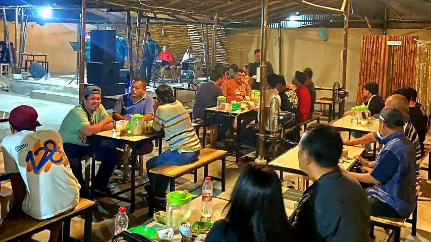 Suasana Kampung Tuak Jalan Bahagia Medan pada malam hari dengan pengunjung menikmati tuak dan live music Batak di bawah atap bambu bernuansa kampung.