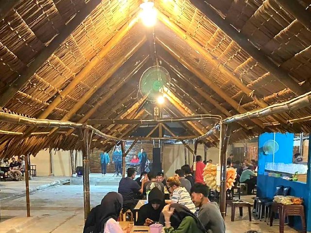 Suasana Kampung Tuak Jalan Bahagia Medan pada malam hari dengan atap rumbia dan pengunjung menikmati tuak sambil menyaksikan live music Batak.