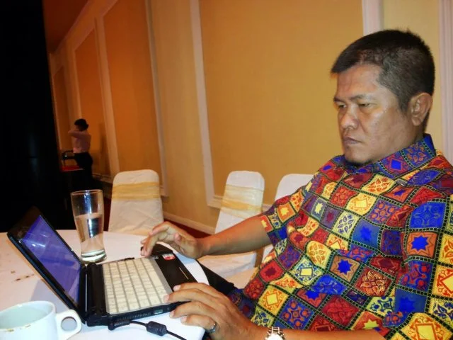 Raja Pardomuan Simbolon sedang bekerja menggunakan laptop saat menghadiri kegiatan di dalam ruangan